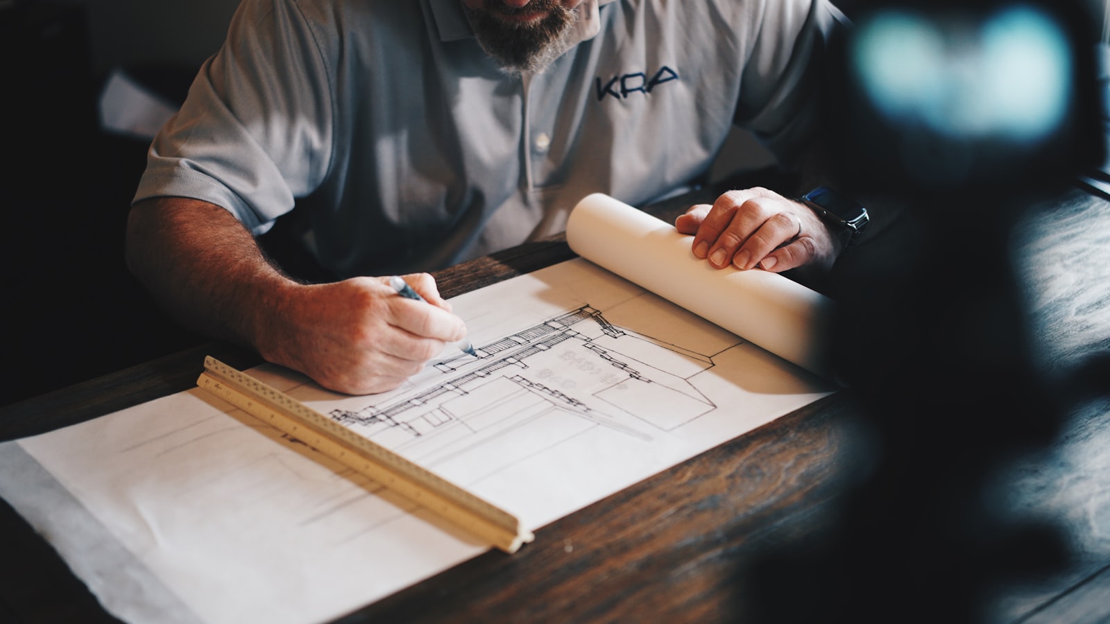 Architectural technologist drafting planning drawings by hand at a desk with a scale rule